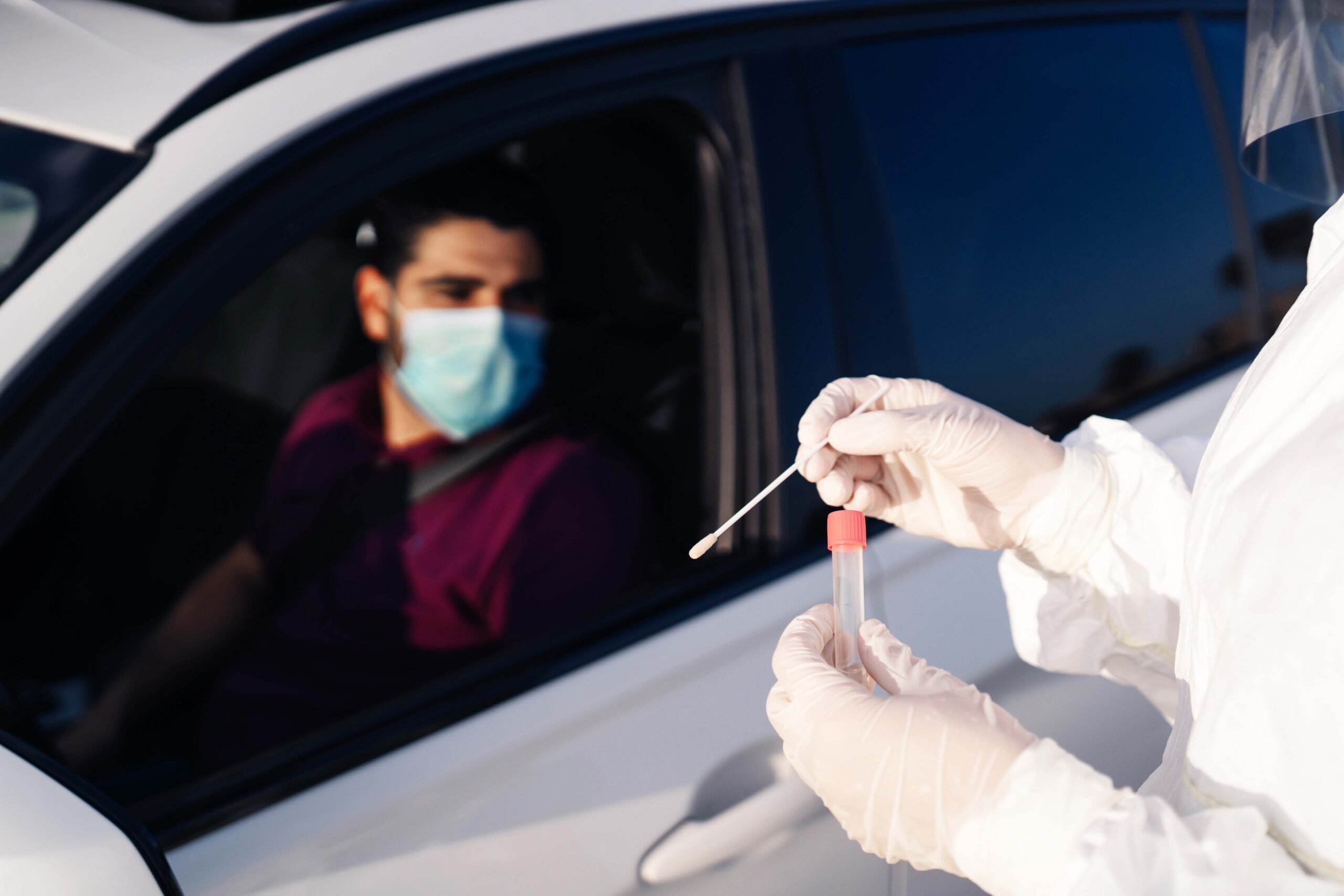 Lab worker collects nasal swab from man driving in a car